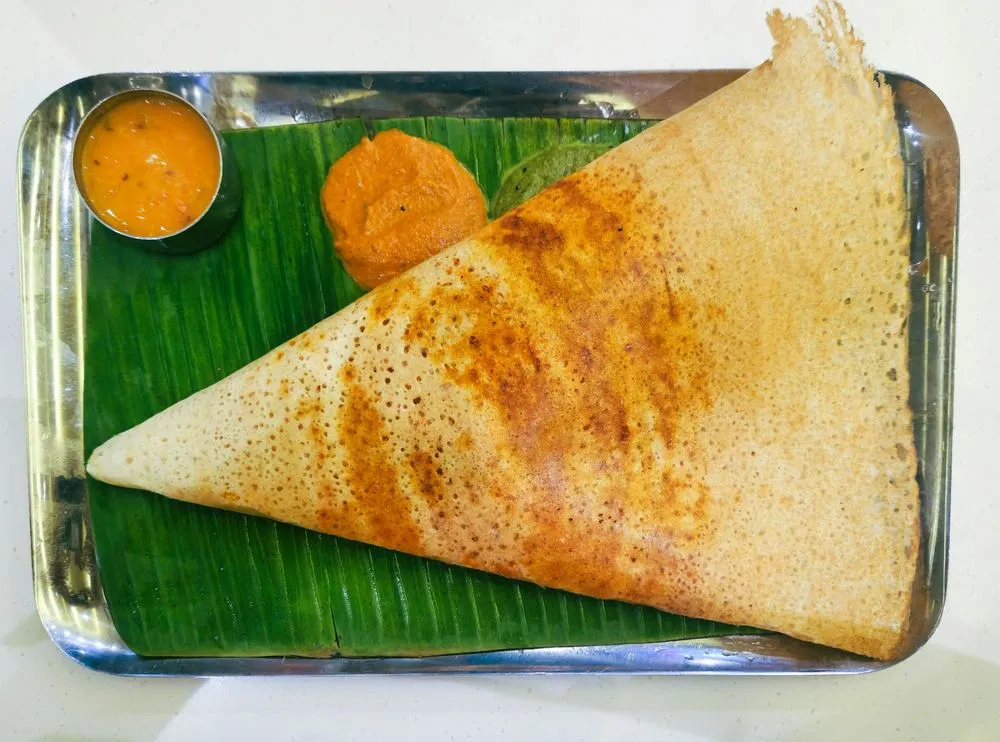A crisp golden dosa on a banana leaf with tomato chutney and sambar