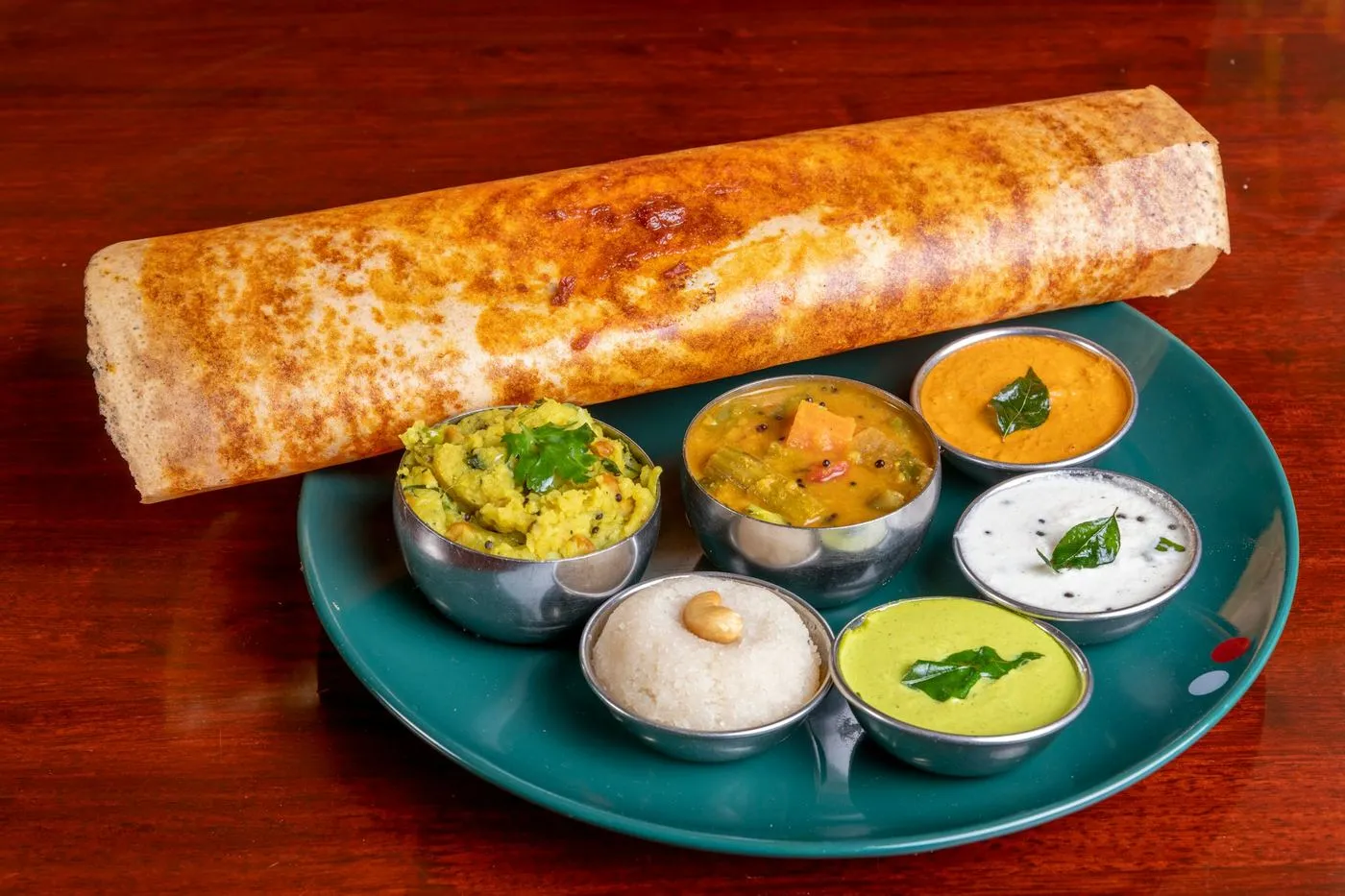 Crispy dosa with sambar and chutneys on a teal plate