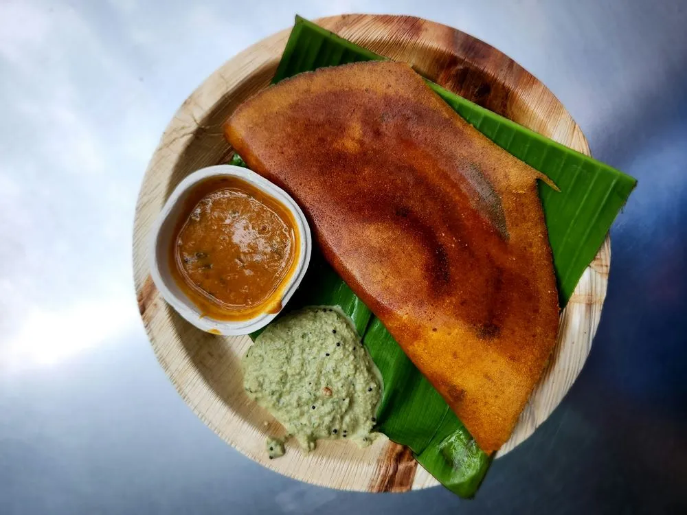 A dosa served on a banana leaf with sambar and coconut chutney