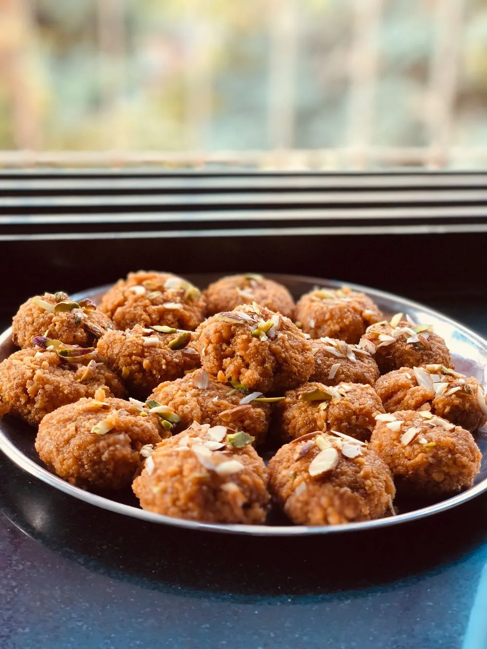 Panjiri-style laddus topped with almond and pistachio slivers on a steel plate